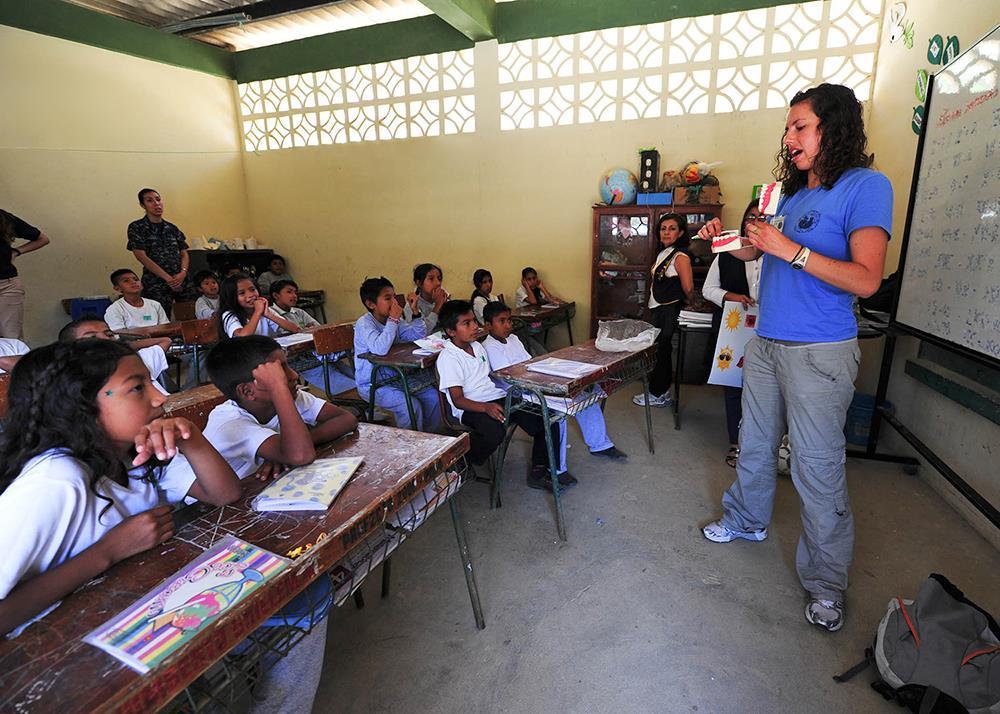 Professora em sala de aula, alunos em carteiras, ambiente de escola pública brasileira