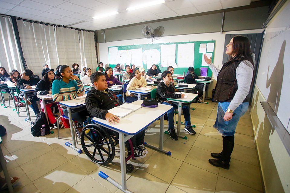 Sala de aula em escola pública, com professora e crianças em ambiente inclusivo e colorido