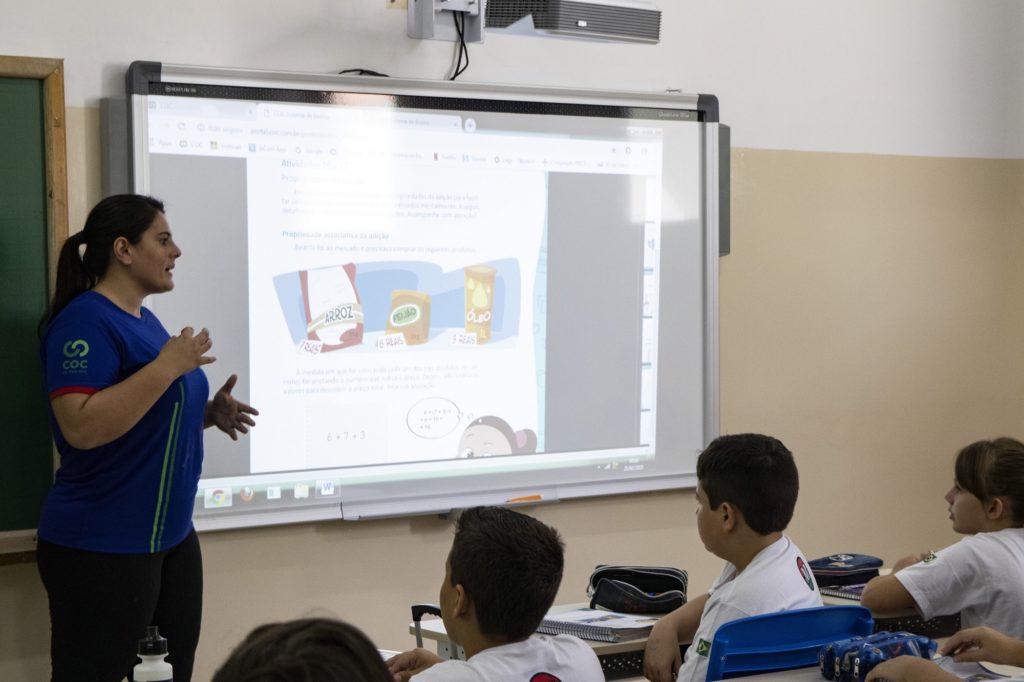 Professora em sala de aula universitária moderna utilizando quadro interativo e projetor, alunos atentos
