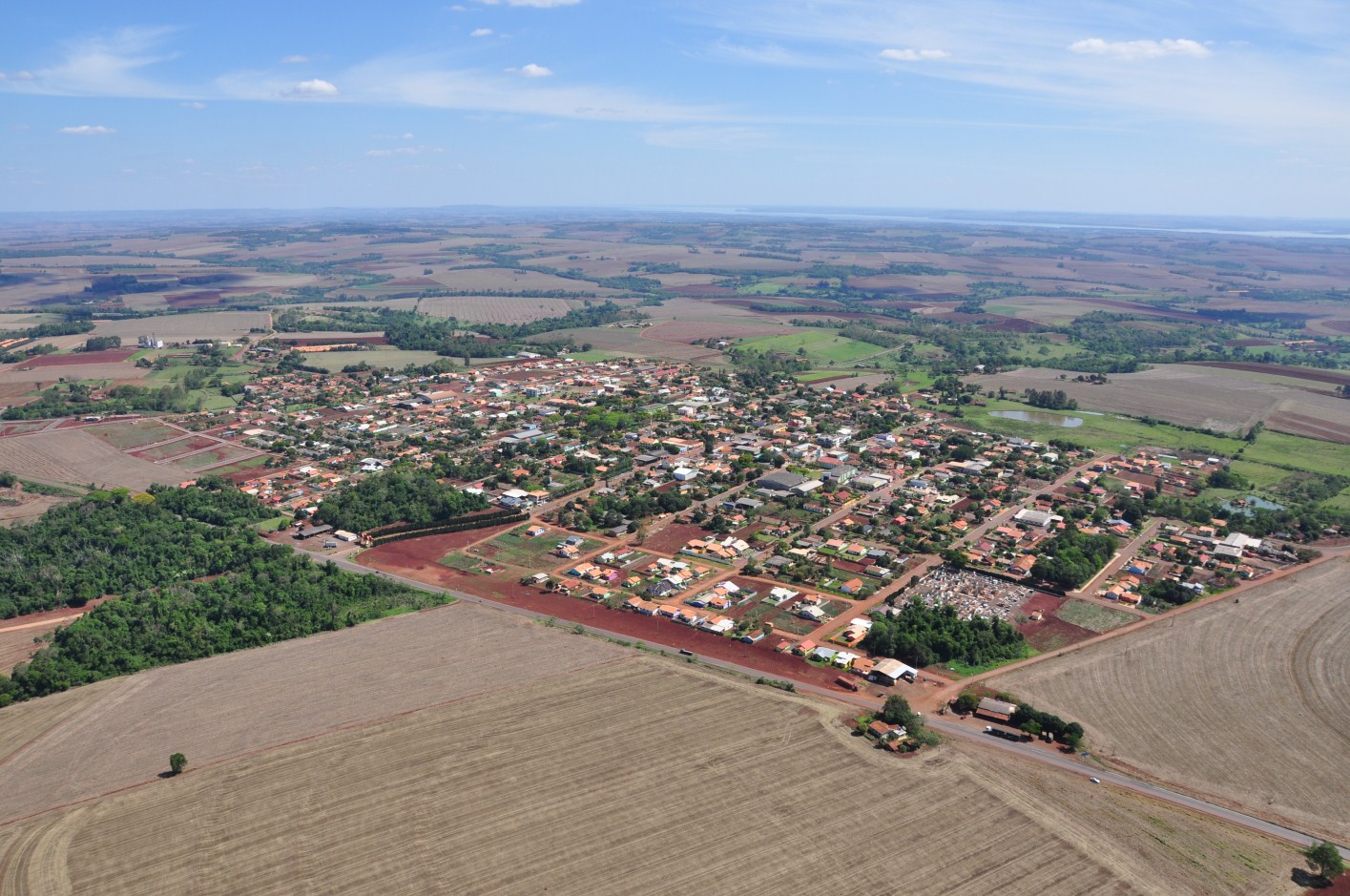 Vista aérea de Mercedes PR, com prédios baixos e ruas em grade; ao redor, áreas agrícolas iluminadas pela luz do fim da tarde.