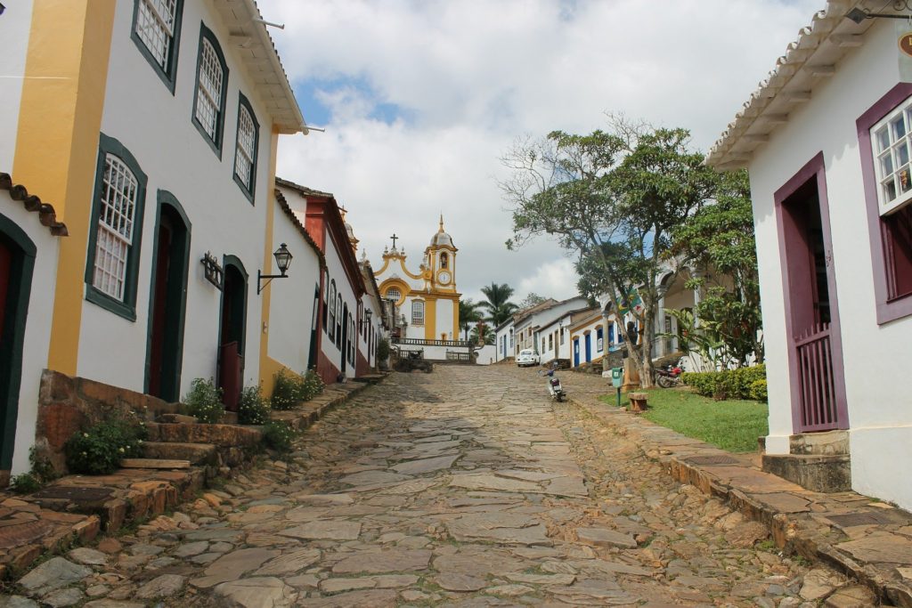 Centro histórico de cidade do interior de Minas Gerais, com casario colonial e igreja ao fundo, em dia claro.