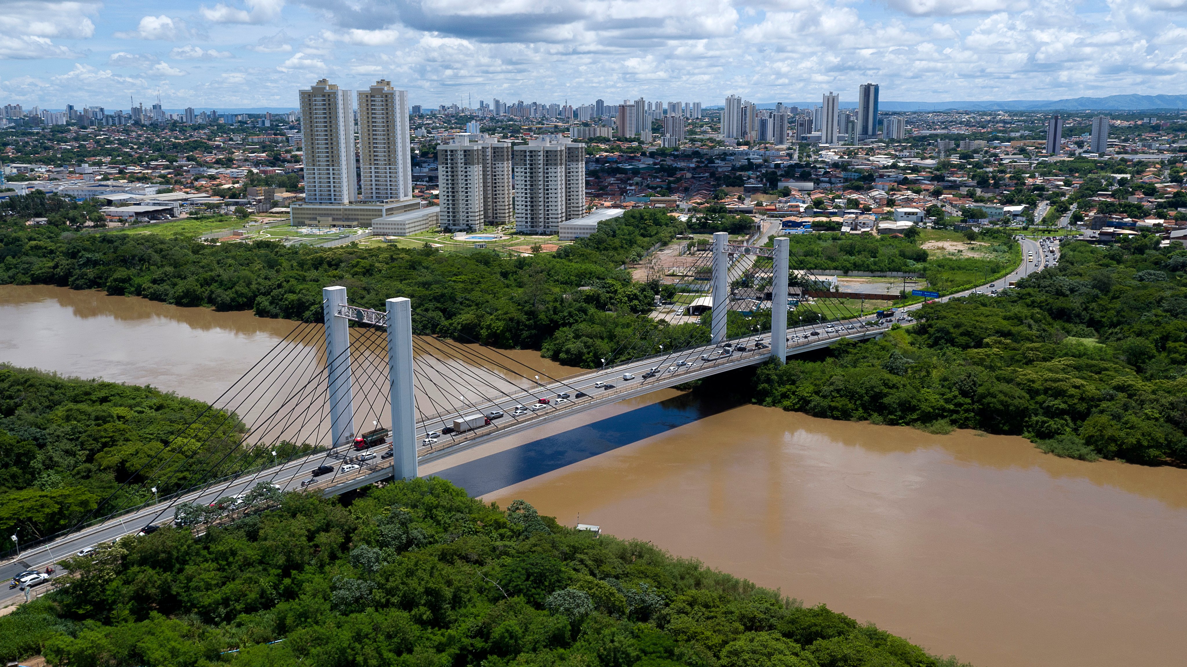Skyline de Cuiabá com rio e ponte ao fundo, em dia ensolarado