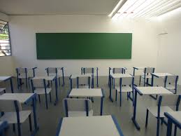 Sala de aula em escola pública, com carteiras enfileiradas e quadro ao fundo, luz natural entrando pelas janelas