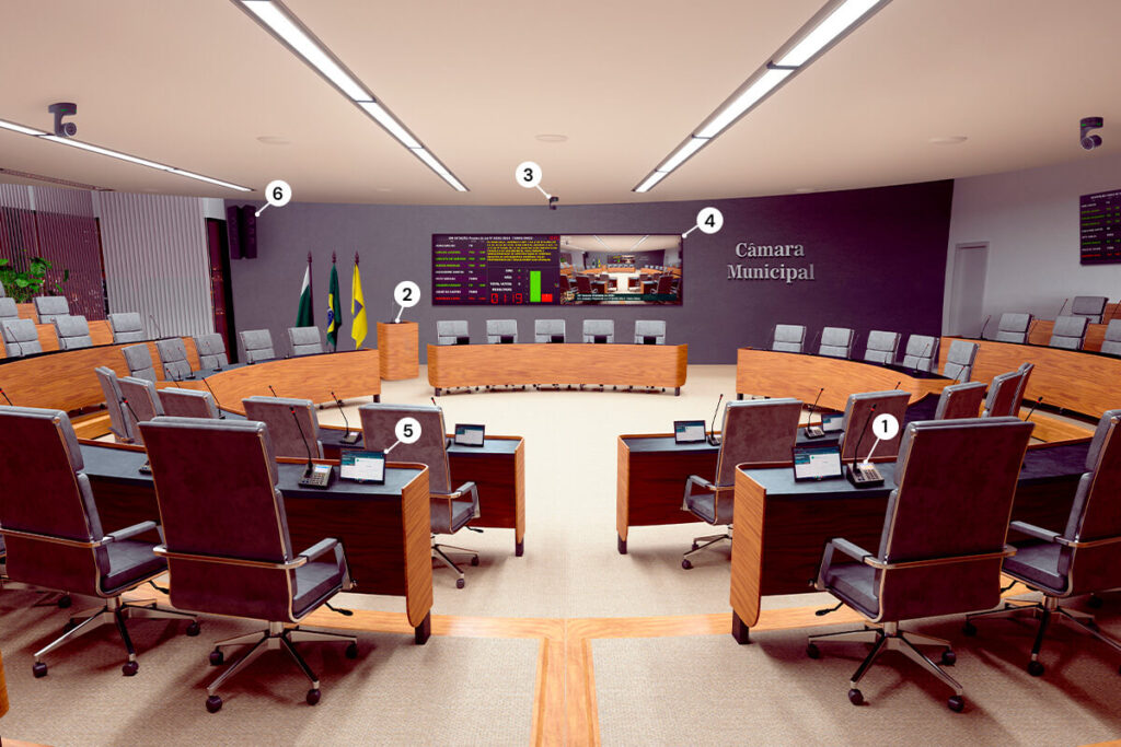 Plenário de câmara municipal, com mesas e microfones, ambiente moderno e iluminado