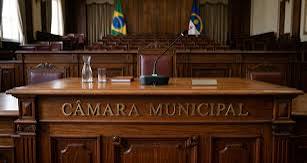 Plenário legislativo municipal com mesa diretora e cadeiras ao fundo