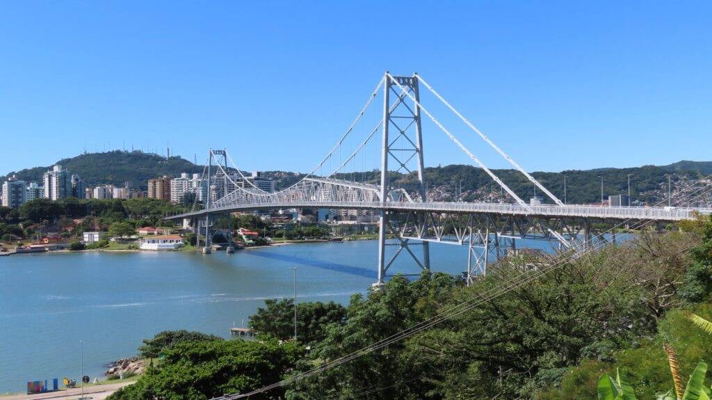 Ponte Hercílio Luz e baía Norte em Florianópolis ao sol, com skyline da cidade ao fundo