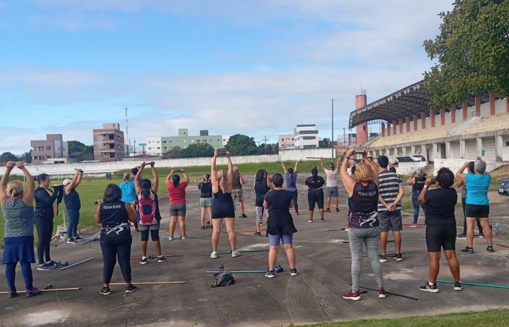 Aula de alongamento em praça pública, com grupo praticando atividade física ao ar livre