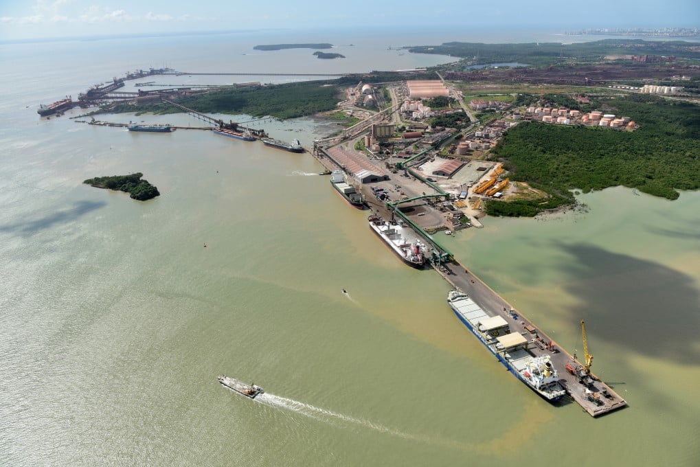 Vista aérea do Porto de Itajaí, com infraestrutura portuária e áreas verdes; a cidade aparece ao fundo sob céu claro.