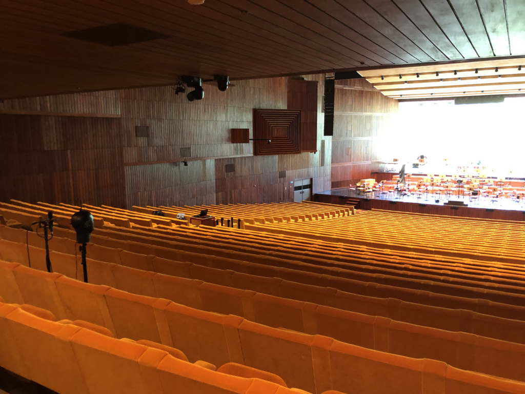 Coro em ensaio com maestro em sala de concerto moderna, luz natural