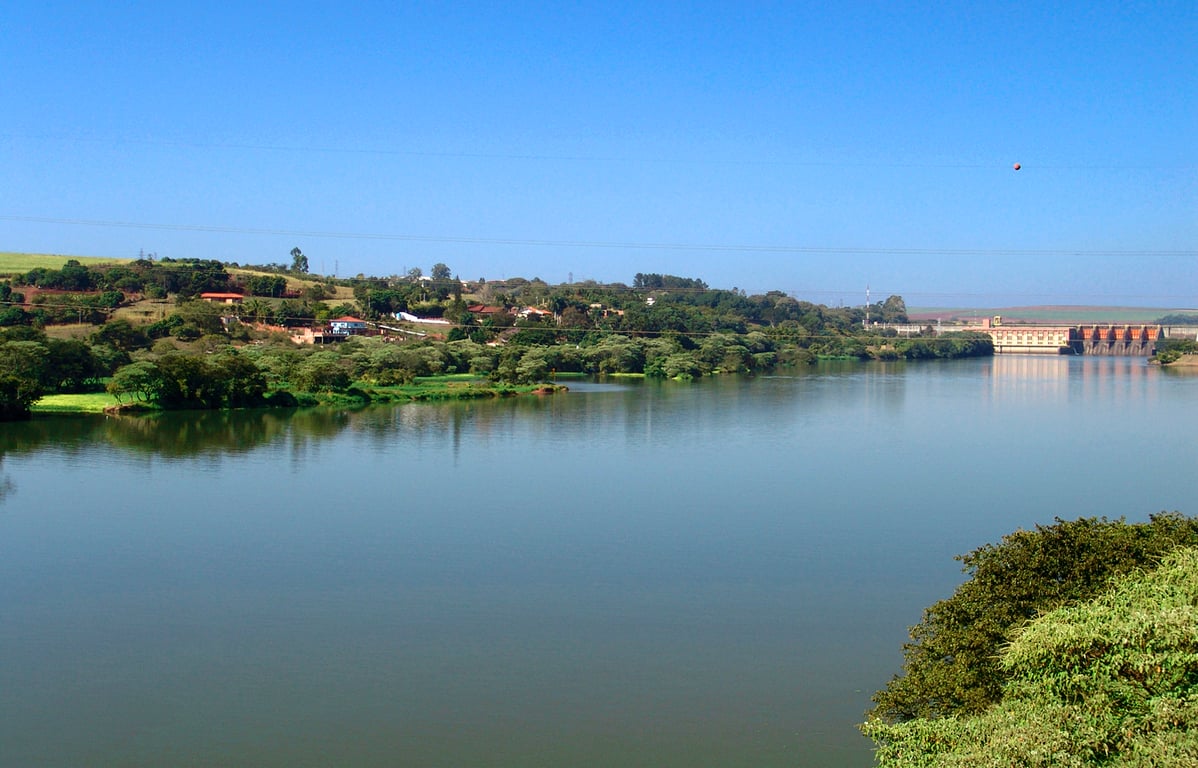 Paisagem de rio largo no interior paulista ao entardecer, com colinas suaves e árvores, remetendo ao Tietê