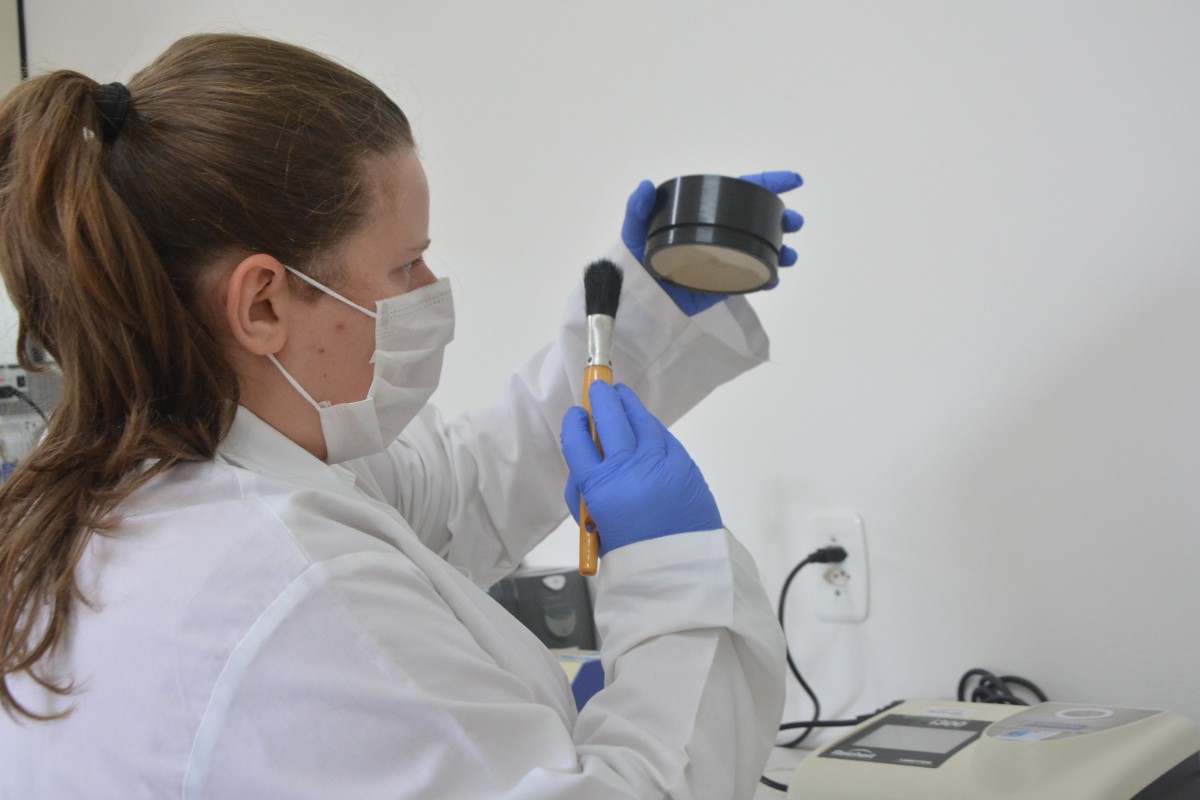 Laboratório de segurança de alimentos com pesquisadora analisando amostras e equipamentos analíticos ao fundo