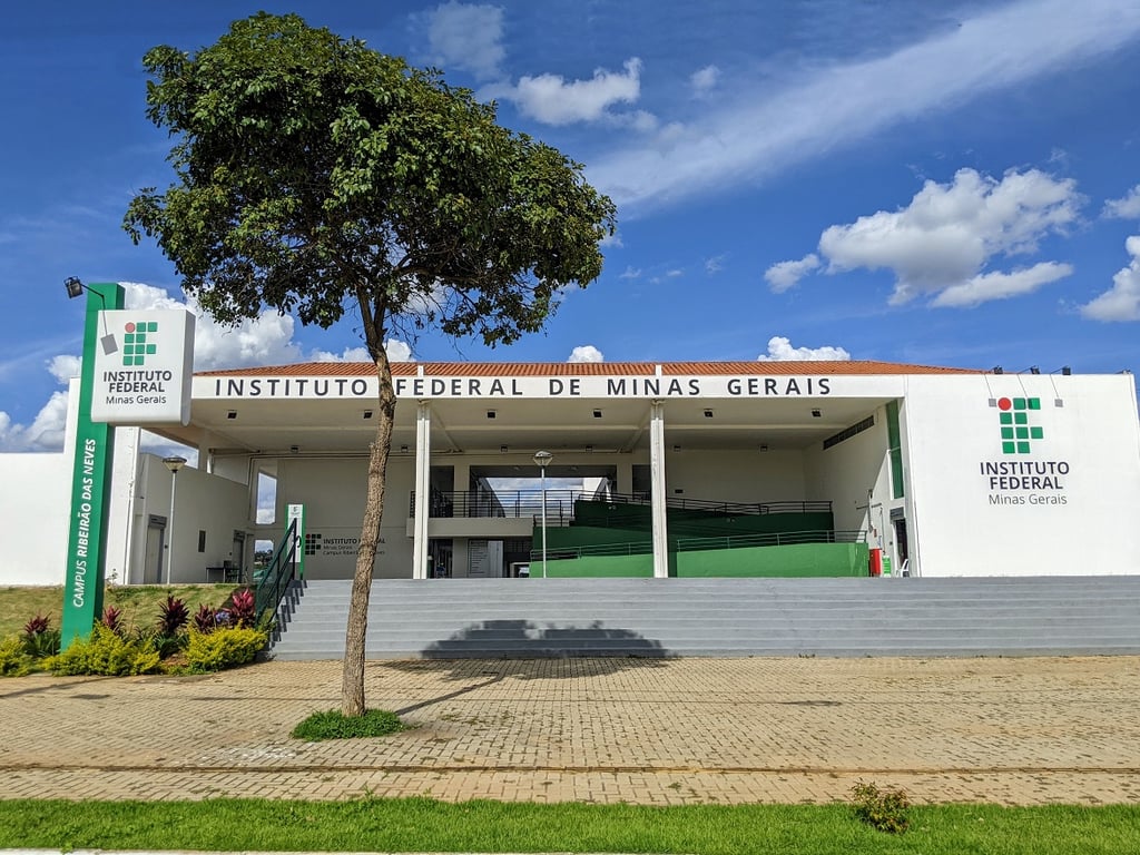 Fachada do IFMG com prédio moderno e vegetação; céu claro ao fundo
