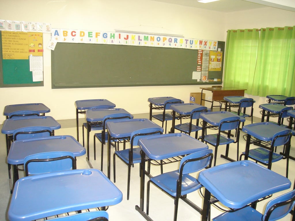 Sala de aula iluminada, com mesas e lousa, em ambiente escolar organizado, foto horizontal estilo editorial