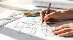 Estudante desenvolvendo projeto de arquitetura em ambiente acadêmico, com mesa de desenho, plantas e maquetes