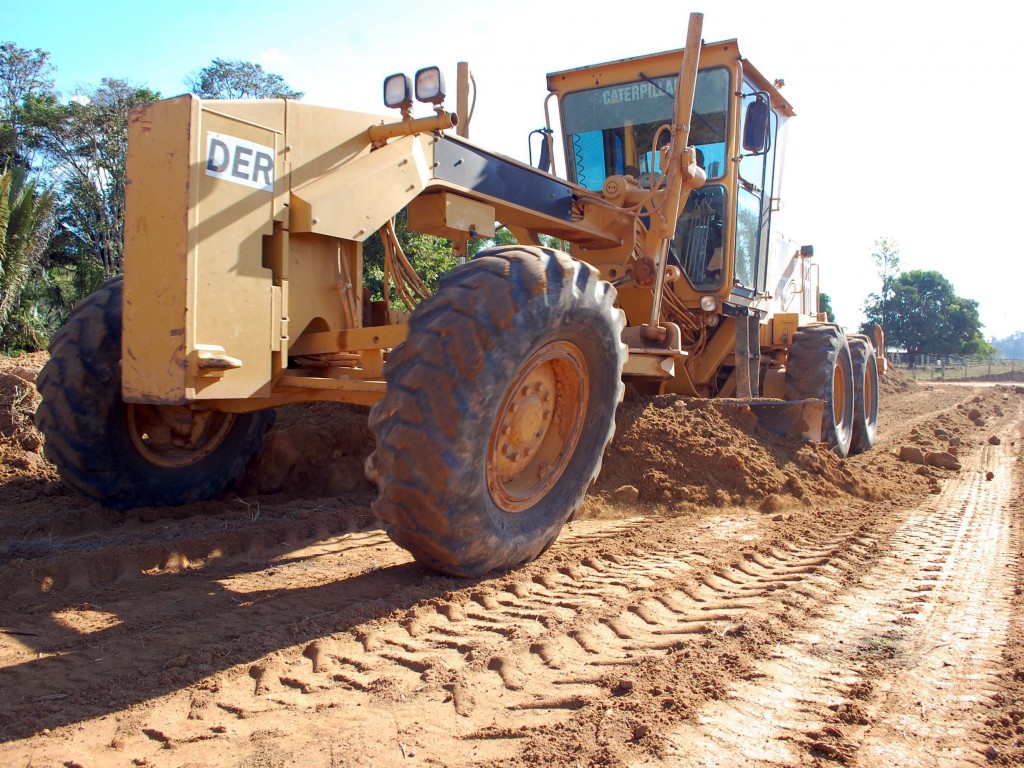 Motoniveladora trabalhando em estrada de terra, céu aberto ao fundo
