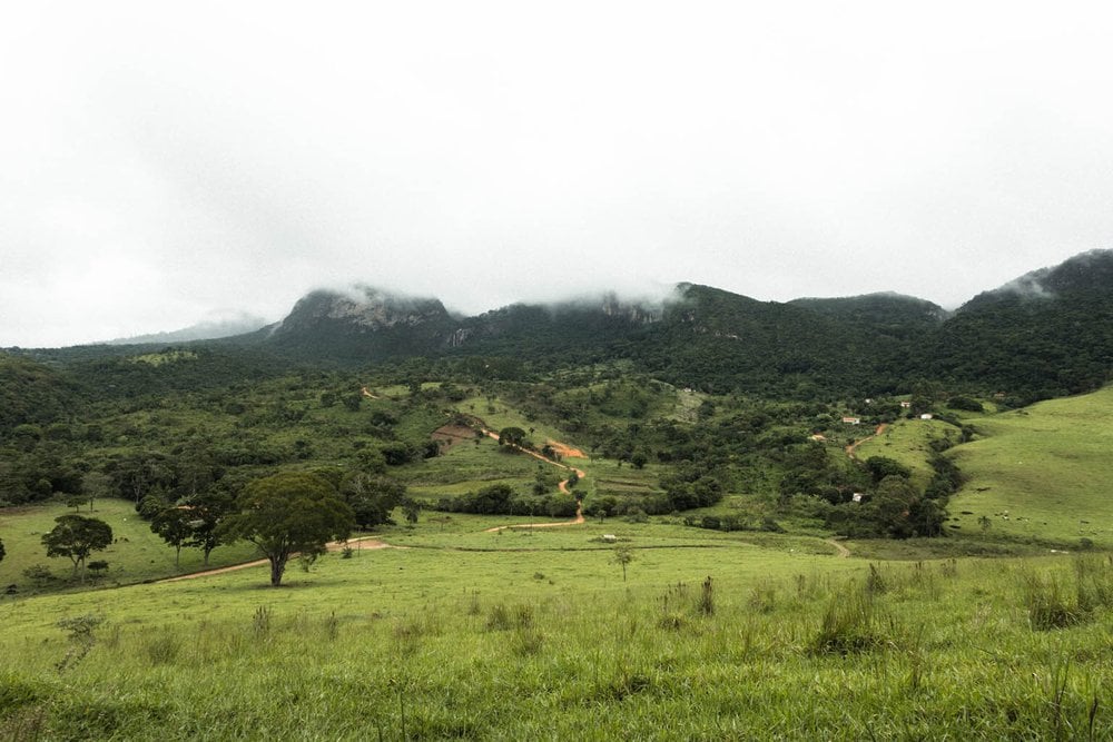 Paisagem de Itabira, Minas Gerais, ao entardecer, com campos verdejantes e montanhas ao fundo