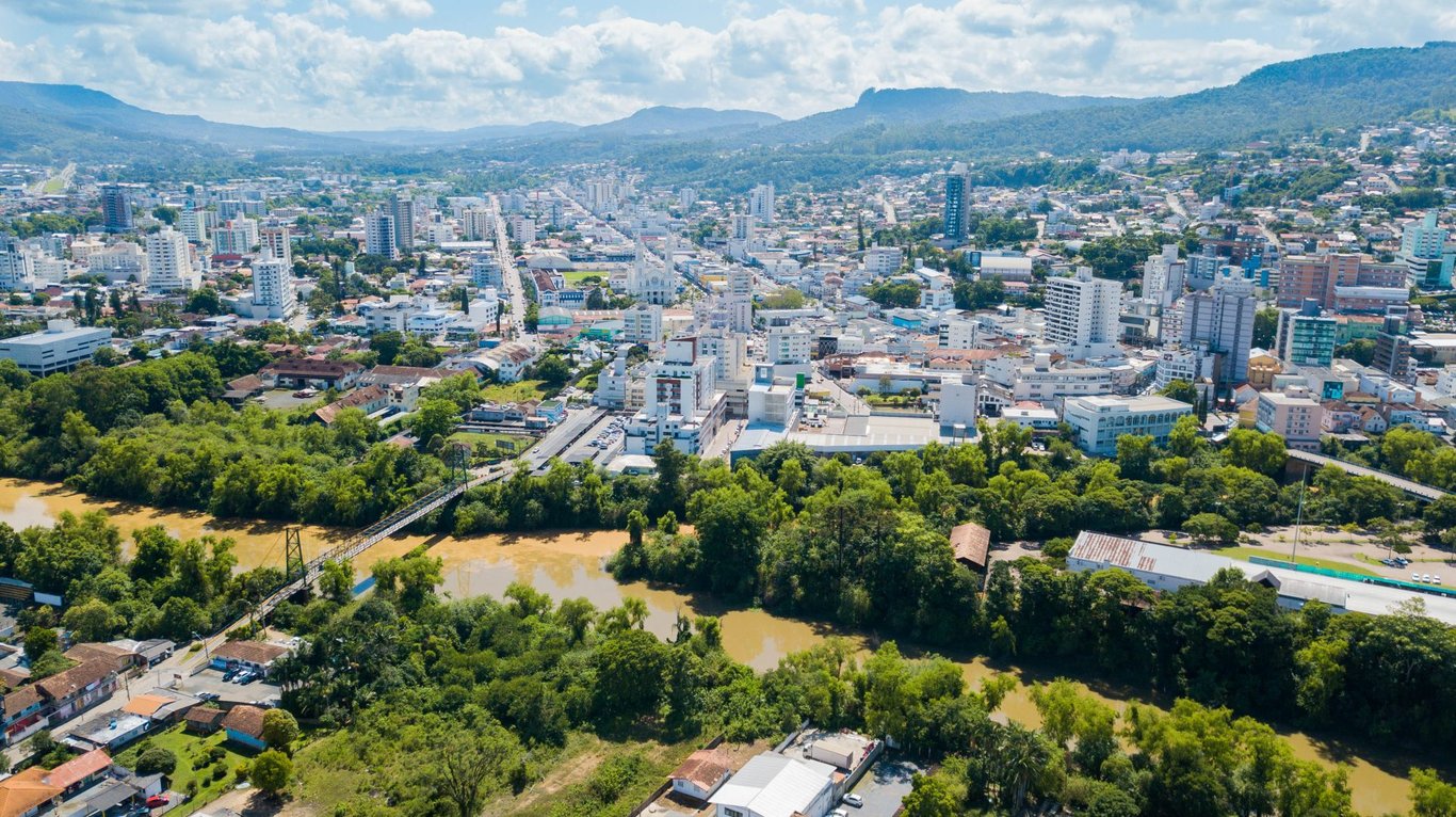 Vista aérea de cidade do interior com rio central e morros ao fundo, típica do Sul do Brasil