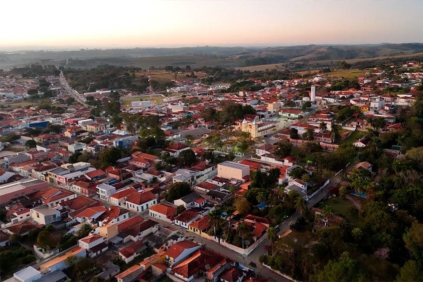 Vista aérea de uma pequena cidade do interior paulista, com ruas, casas e áreas verdes ao redor