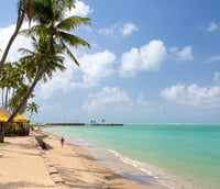Vista da orla de Maceió, com mar turquesa e palmeiras ao pôr do sol.