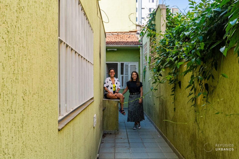 Corredor urbano com vegetação e duas pessoas; logotipo “Refúgios Urbanos” no canto inferior direito
