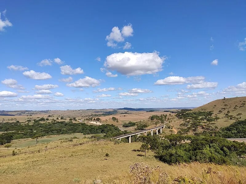 Paisagem do Oeste catarinense, com estrada e morros ao fundo sob céu aberto. Imagem ilustrativa.