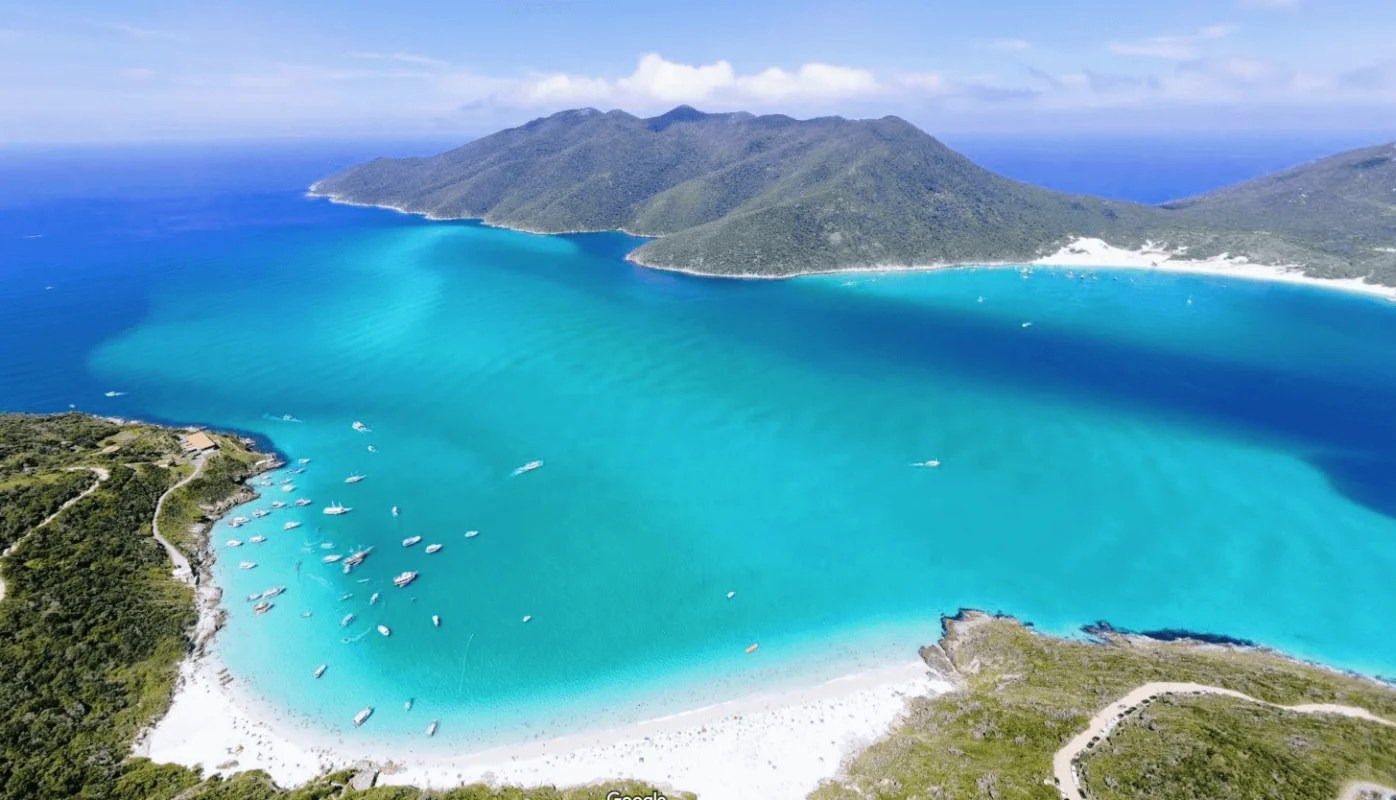Vista aérea da orla de Arraial do Cabo RJ, com mar azul-turquesa, barcos e faixa de areia clara