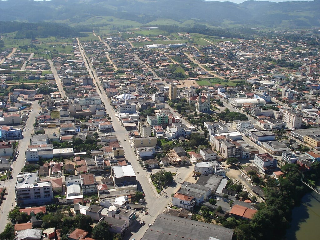 Vista aérea de cidade pequena em região serrana do Vale do Braço do Norte, com morros e vegetação ao fundo
