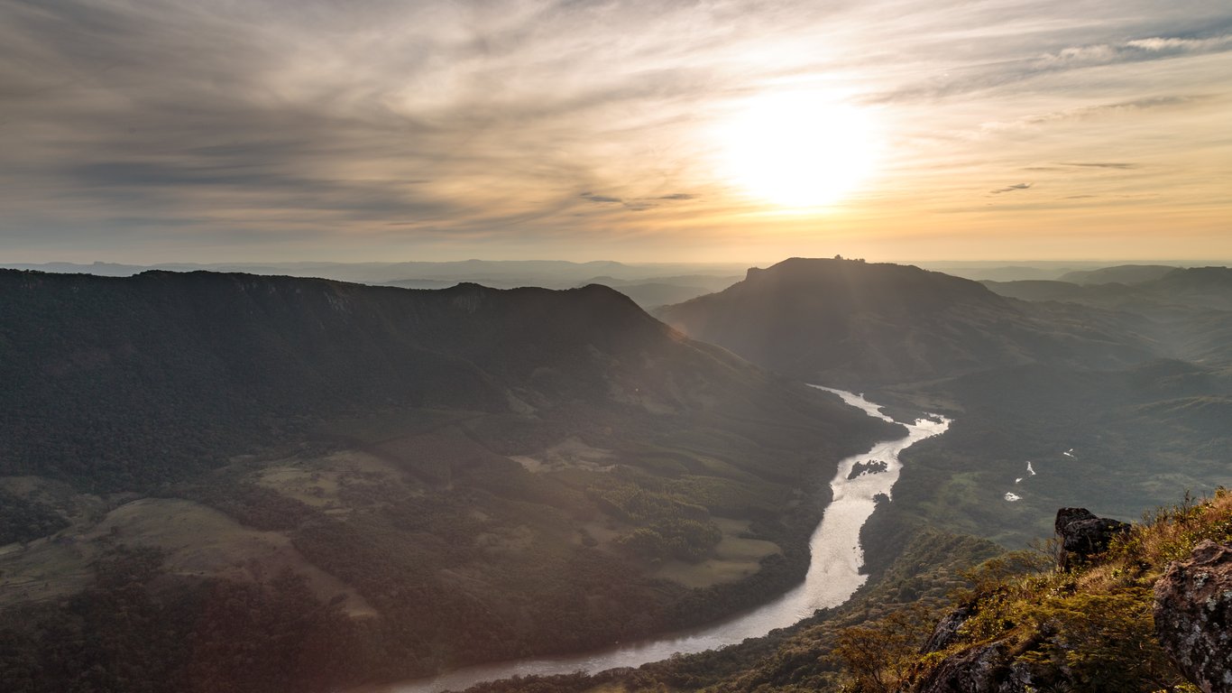Vista panorâmica do Pico Agudo ao pôr do sol, em Sapopema (PR), com morros verdes e horizonte amplo
