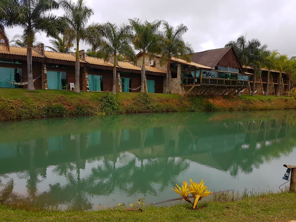 Paisagem de cidade do interior com lago, palmeiras e construções de madeira, ao entardecer