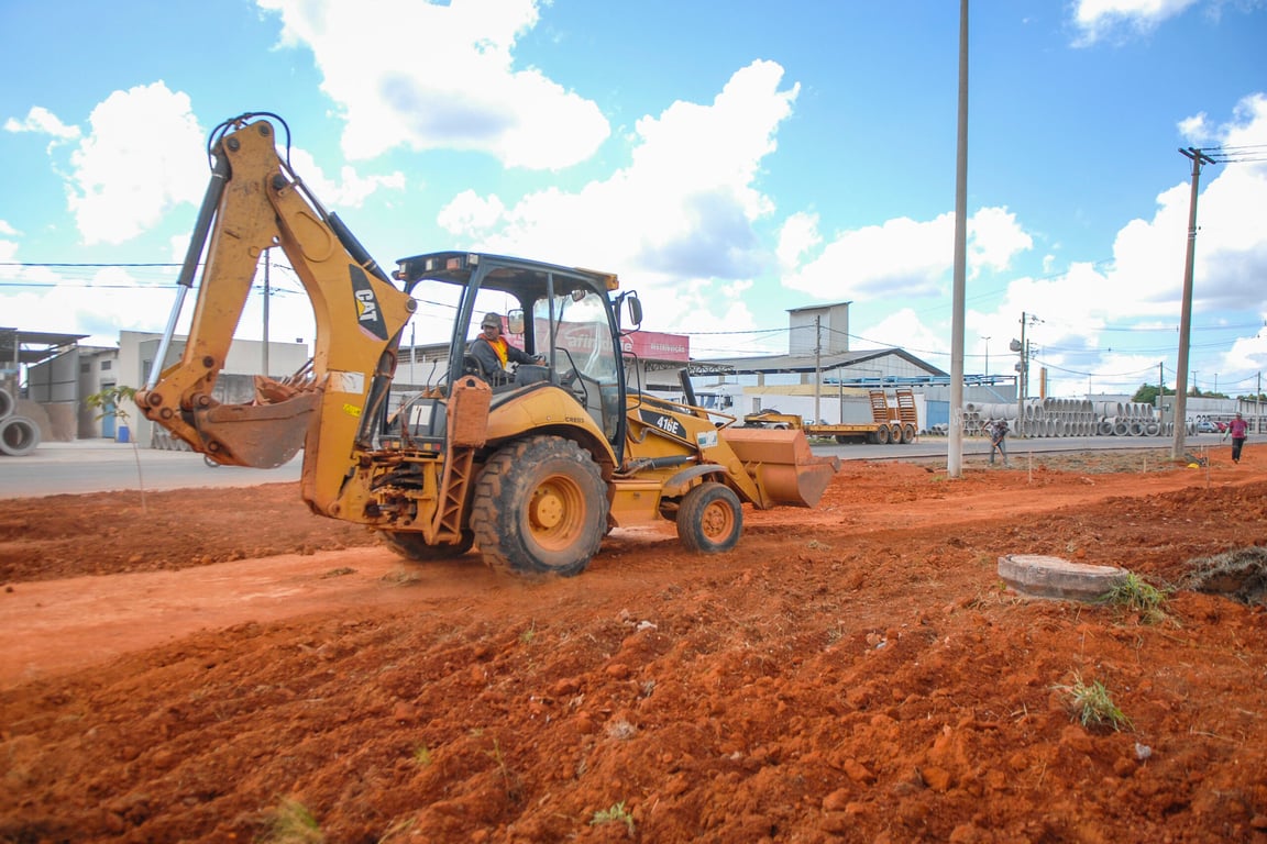 Motoniveladora em estrada rural de terra, com céu azul e nuvens ao fundo