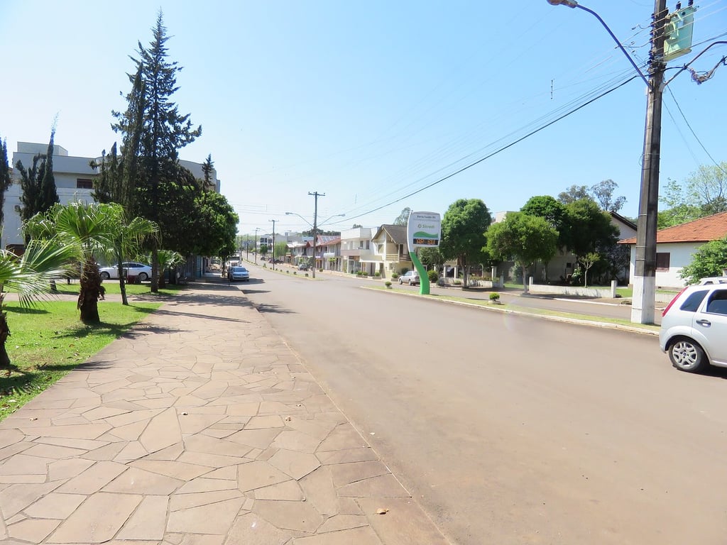 Rua arborizada em Barra Funda RS, em dia ensolarado, com casas e calçadas simples, representando o cotidiano do município