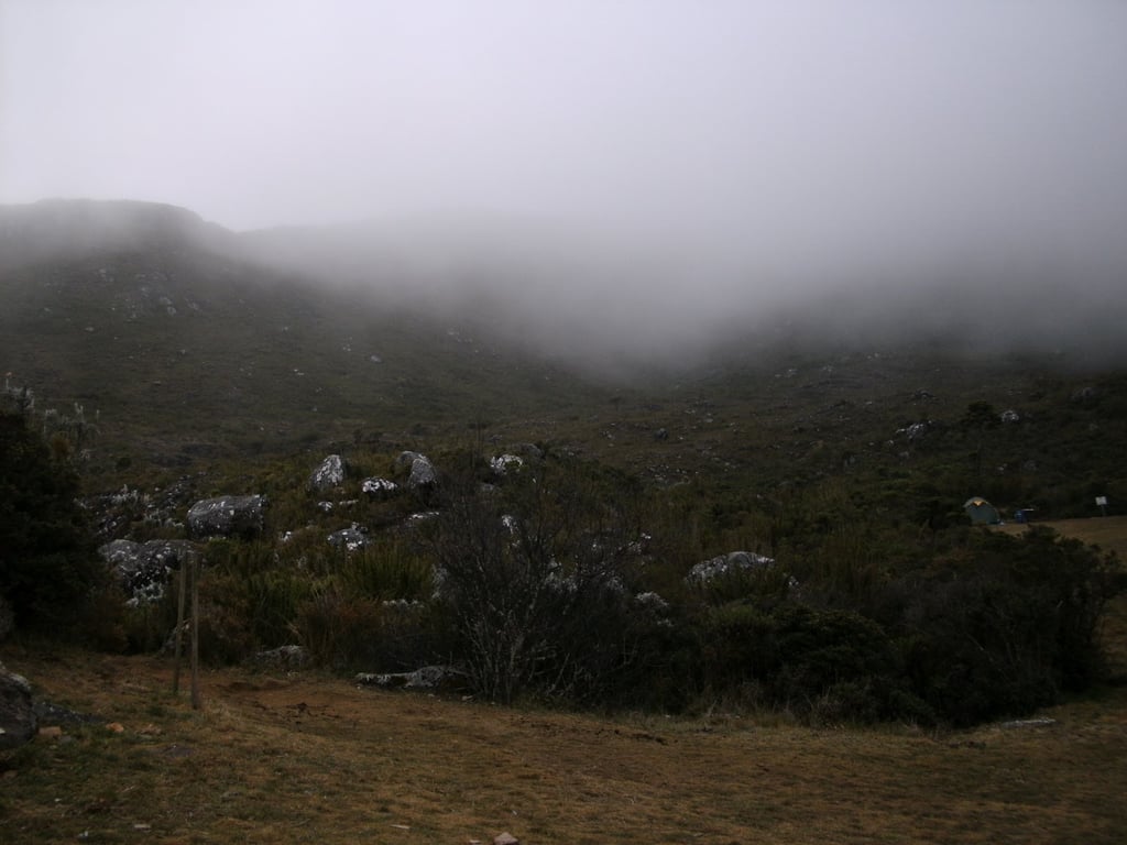 Montanhas da região do Caparaó com vegetação e névoa ao fundo; luz suave de fim de tarde