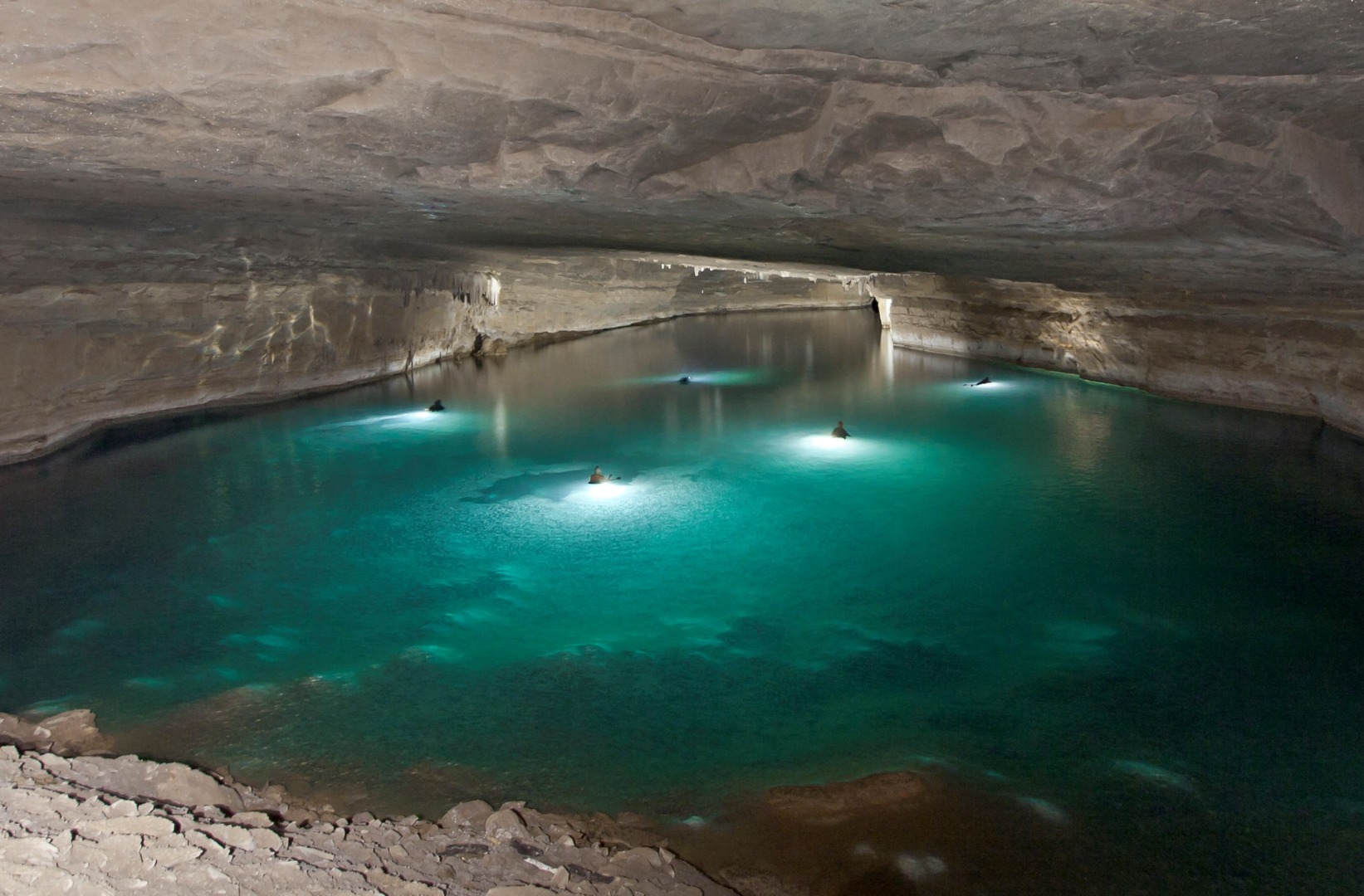 Caverna com lago e feixes de luz natural, paredões e formações rochosas no oeste da Bahia