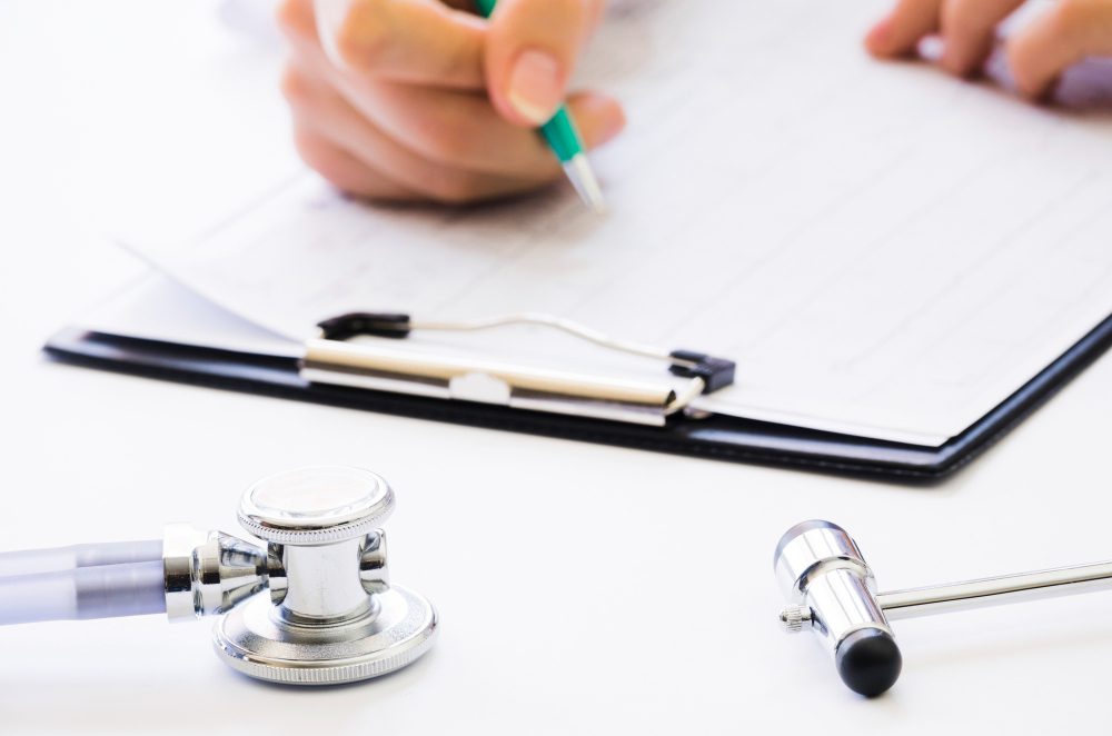 Médico preenchendo laudo pericial em consultório, com prancheta e estetoscópio sobre a mesa