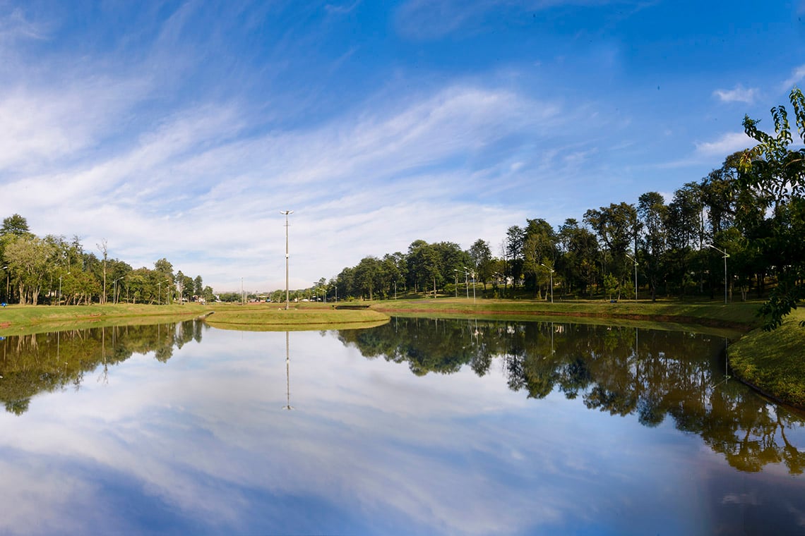 Paisagem urbana tranquila no Sudoeste do Paraná, com lago e árvores refletidas sob céu aberto