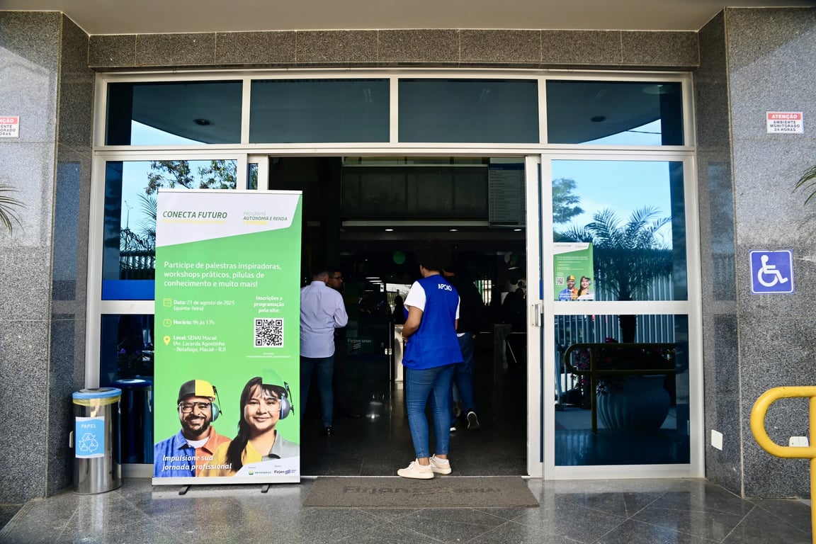 Ambiente educacional com circulação de estudantes, banner de evento e pessoas entrando em prédio