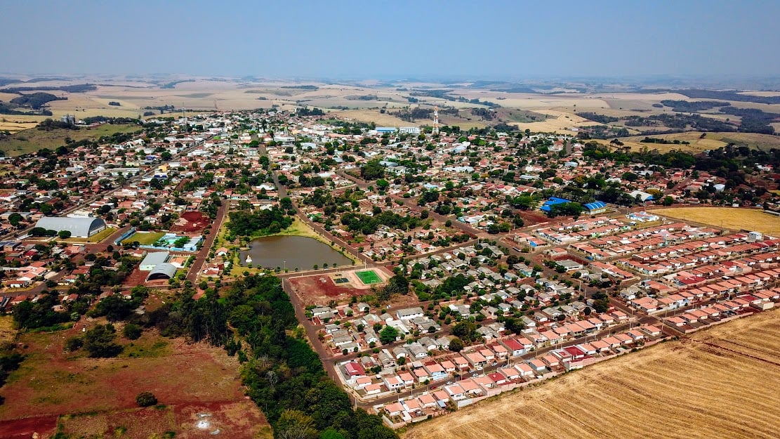 Vista aérea do centro urbano de Borrazópolis PR, com quarteirões arborizados e lagoa em dia ensolarado.