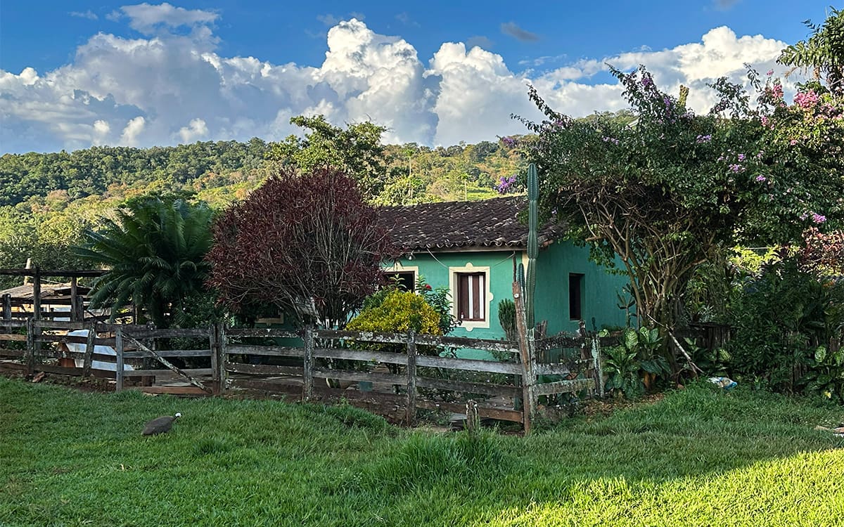 Paisagem do Cerrado goiano com casa rural ao fundo e céu azul, em orientação horizontal.