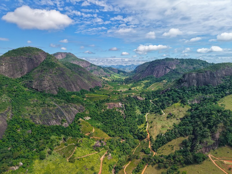 Paisagem de município do interior capixaba, com morros verdes e estrada vicinal sob céu azul