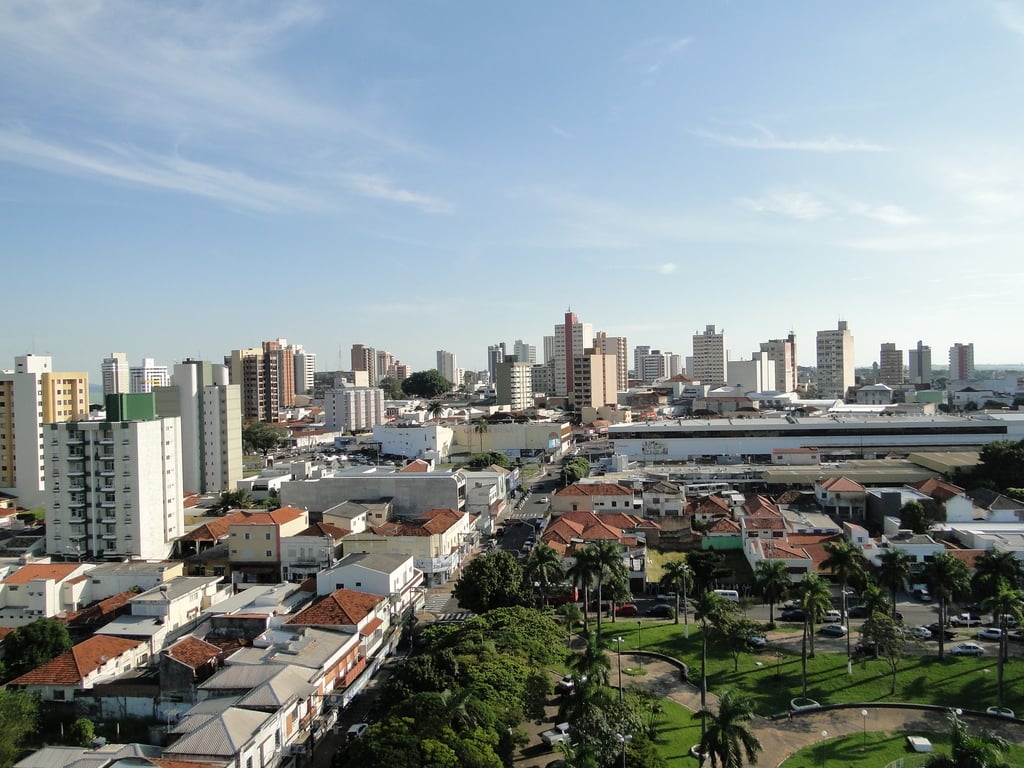 Vista urbana de cidade do interior de SP, com avenida arborizada e prédios baixos sob céu aberto