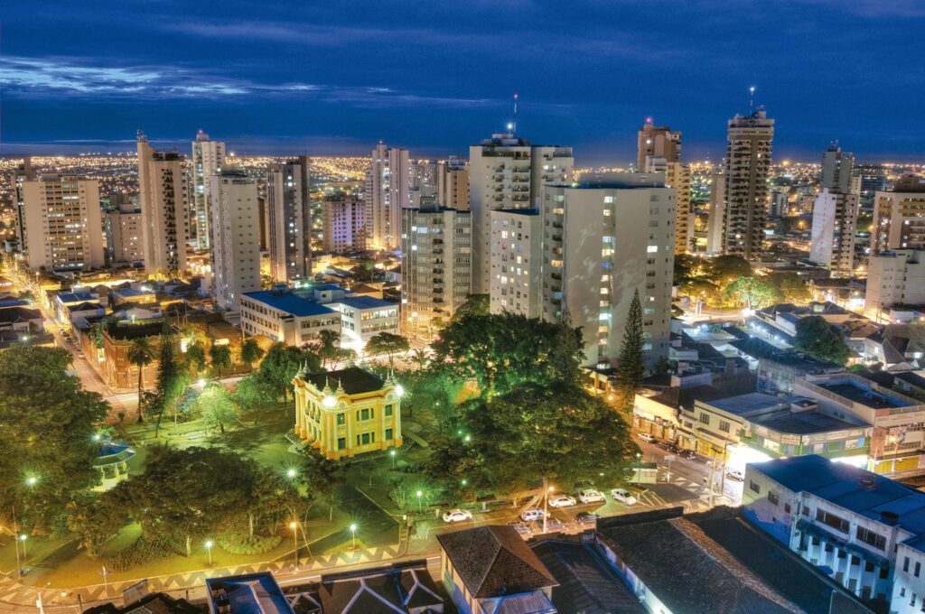 Vista aérea de Uberlândia à noite, com skyline iluminado e áreas verdes ao fundo