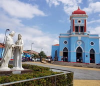 Vista do Santuário de São José de Ribamar à beira-mar, céu azul e esculturas em primeiro plano.