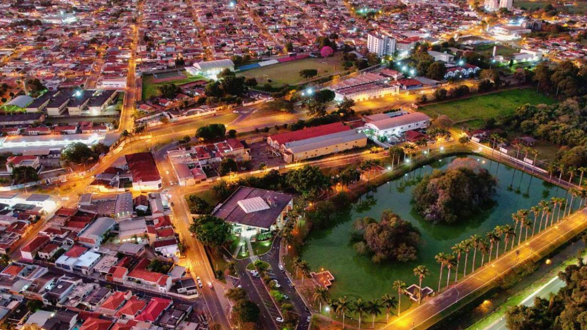 Vista aérea noturna de Jaboticabal, com lago, palmeiras e área urbana iluminada