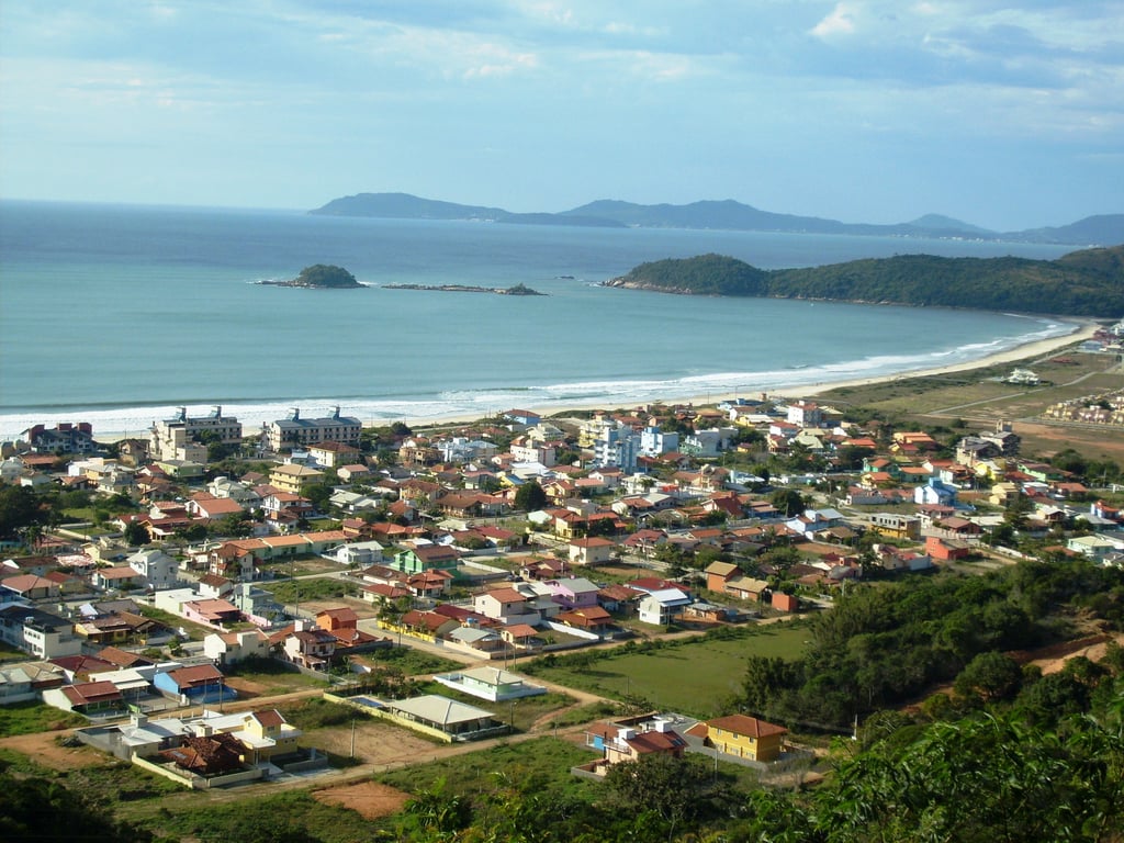 Vista aérea da Praia de Palmas, mar azul e faixa de areia com morros ao fundo, em Governador Celso Ramos SC