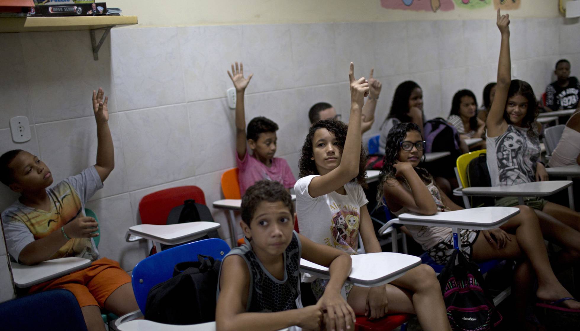 Foto de sala de aula com alunos levantando as mãos durante uma atividade em grupo.