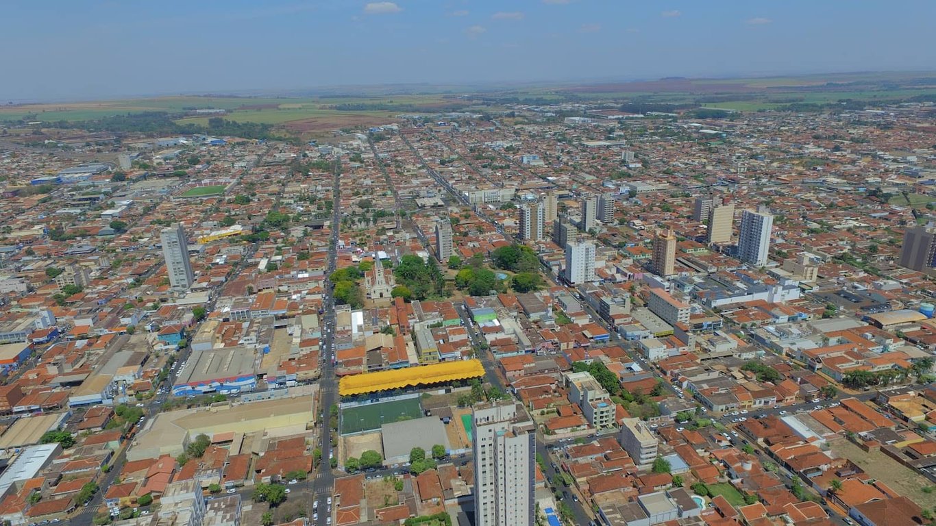 Foto aérea de Sertãozinho, São Paulo, com urbanização de baixo gabarito e áreas verdes sob céu claro.