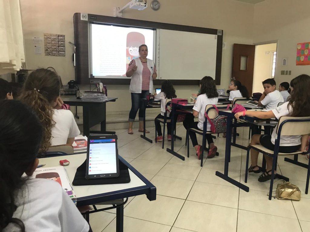 Sala de aula com tecnologia educacional: estudantes usando tablets com mediação da professora