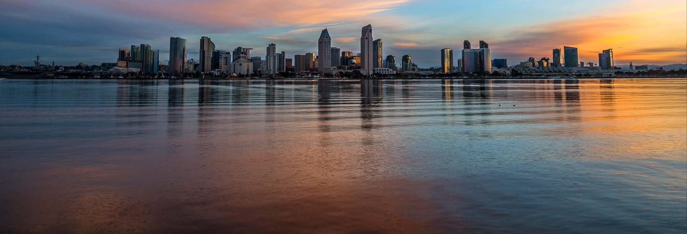 Imagem ilustrativa de skyline urbano ao entardecer, com prédios refletidos na água
