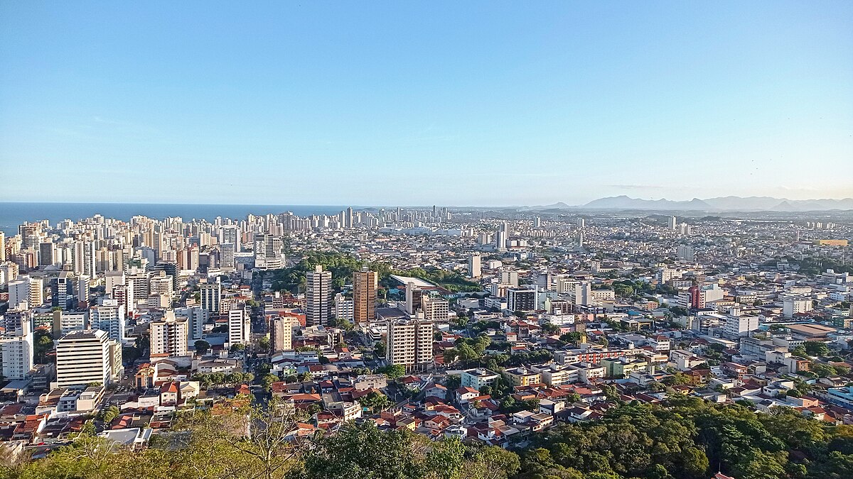 Vista de cidade com serras ao fundo, em composição horizontal