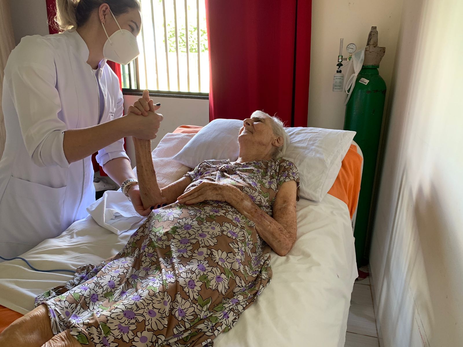 Atendimento domiciliar com profissional de enfermagem ao lado de paciente idosa em ambiente residencial